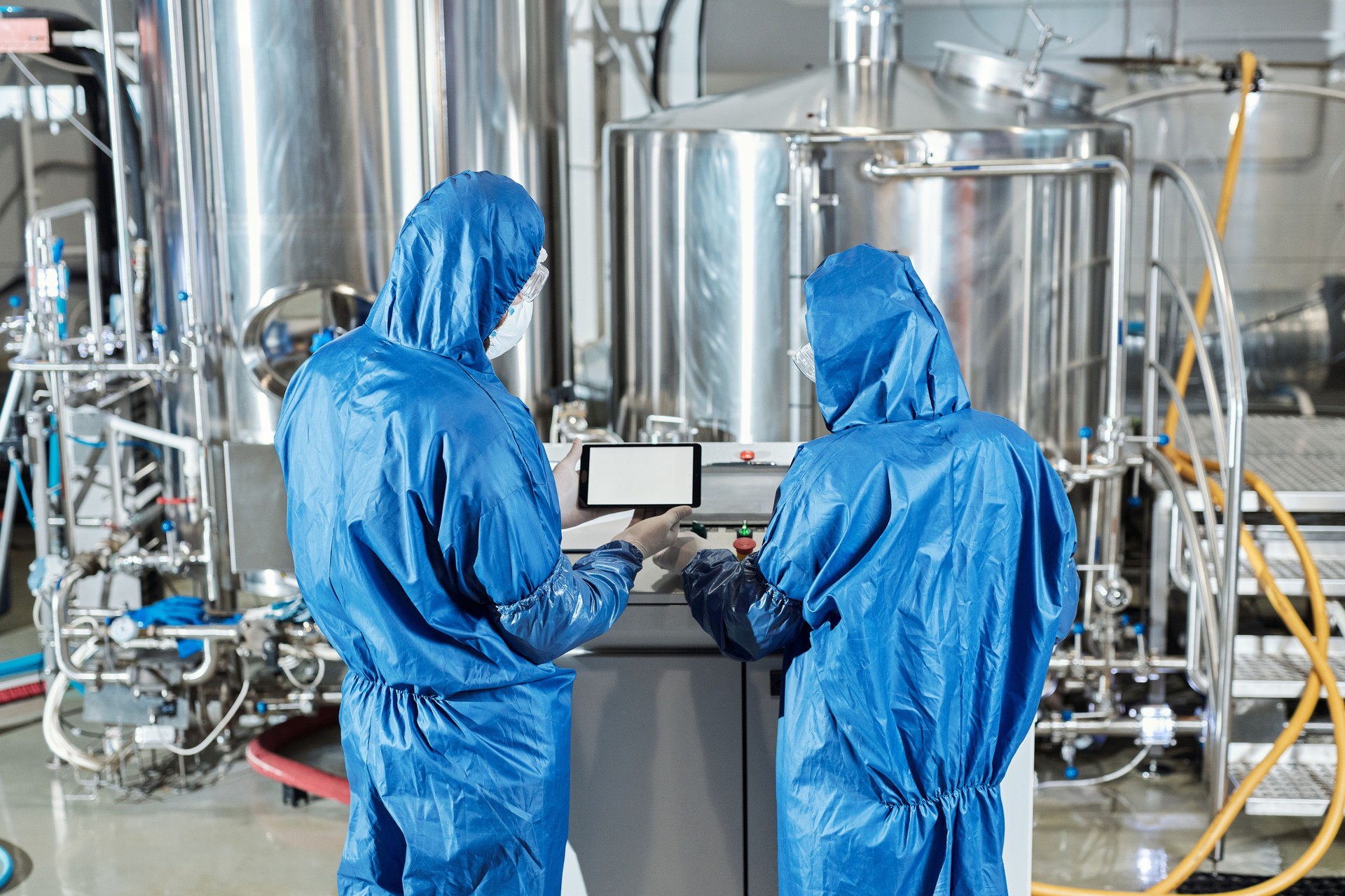 Back view of two workers using control panel at chemical factory